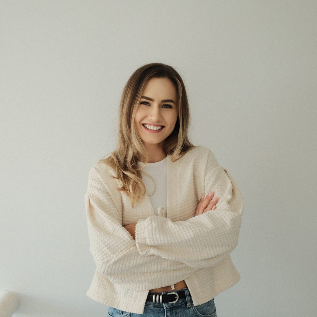 Iza Ledzka, smiling with her arms crossed, in a cream sweater.